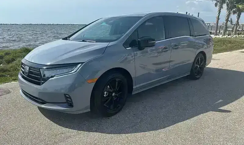 A 2024 Honda Odyssey from the SWFL Auto Rentals fleet, parked on a paved road beside the water