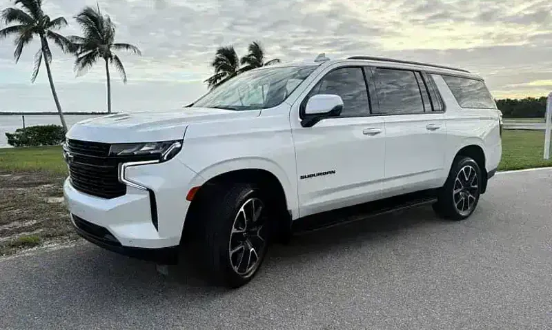 A 2023 Chevrolet Suburban from the SWFL Auto Rentals fleet, parked on a coastal road at sunset